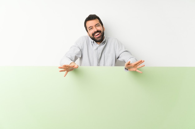 Hombre guapo joven con barba sosteniendo un gran cartel verde vacío sonriendo