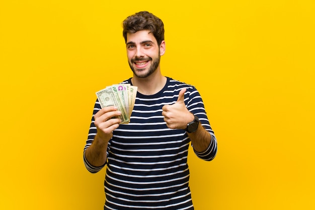 Hombre guapo joven con billetes de dólar contra backgrou naranja