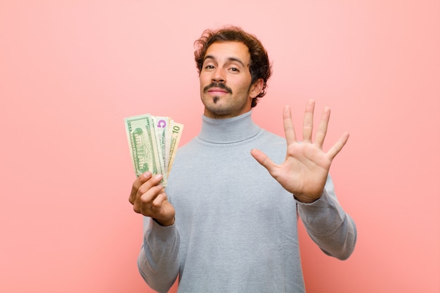 Hombre guapo joven con billetes de dólar contra la pared plana rosa