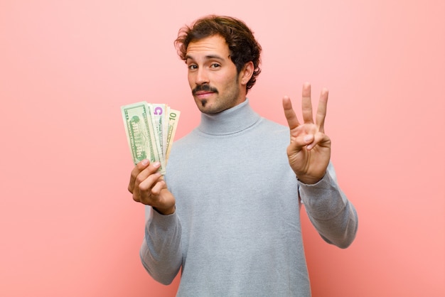 Hombre guapo joven con billetes de dólar contra la pared plana rosa