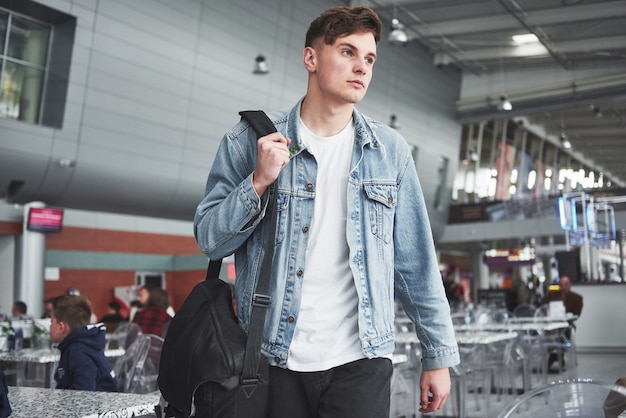 Hombre guapo joven con una bolsa en el hombro a toda prisa hacia el aeropuerto.