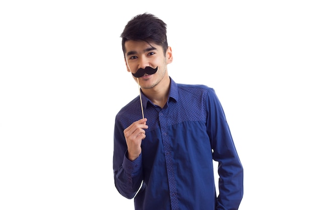 Hombre guapo joven con cabello oscuro en camisa azul con palo de cartón de bigote en estudio