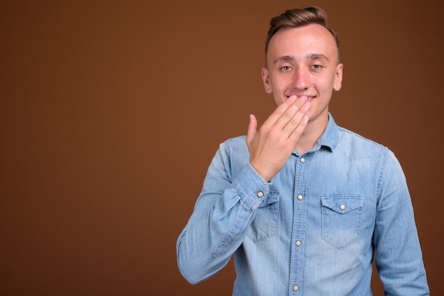 Hombre guapo joven con cabello rubio contra la pared marrón