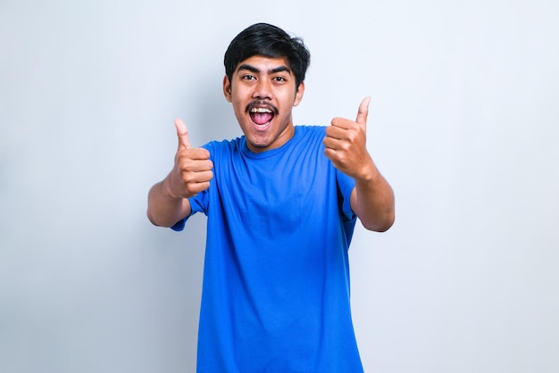 Hombre guapo joven con camisa casual sobre fondo blanco aprobando hacer un gesto positivo con la mano, pulgar hacia arriba sonriendo y feliz por el éxito. Gesto de ganador.