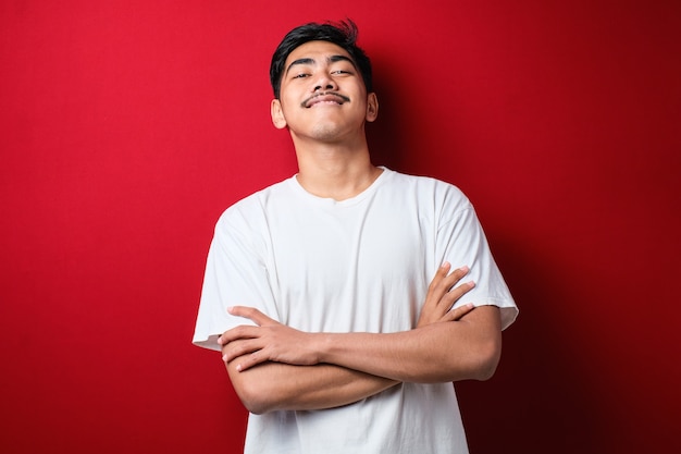 Hombre guapo joven con camisa casual sobre fondo rojo cara feliz sonriendo con los brazos cruzados mirando a la cámara. persona positiva.