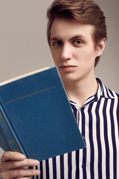 Hombre guapo joven en camisa a rayas leyendo un libro en gris