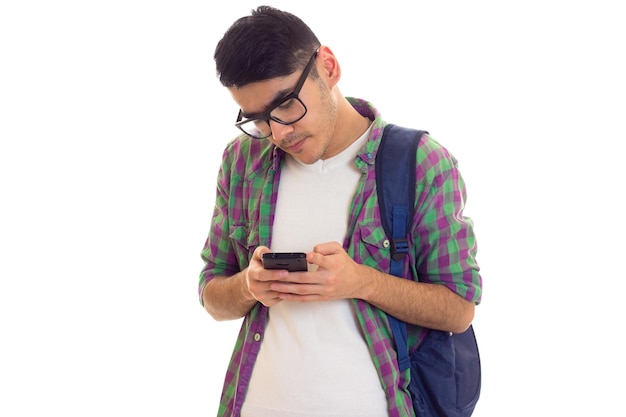 Hombre guapo joven en camiseta blanca y camisa a cuadros con mochila azul usando su teléfono inteligente