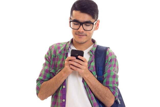 Hombre guapo joven en camiseta blanca y camisa a cuadros con mochila azul usando su teléfono inteligente