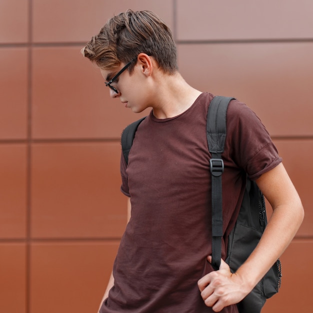 Hombre guapo joven con una camiseta y gafas de sol, sosteniendo una mochila.