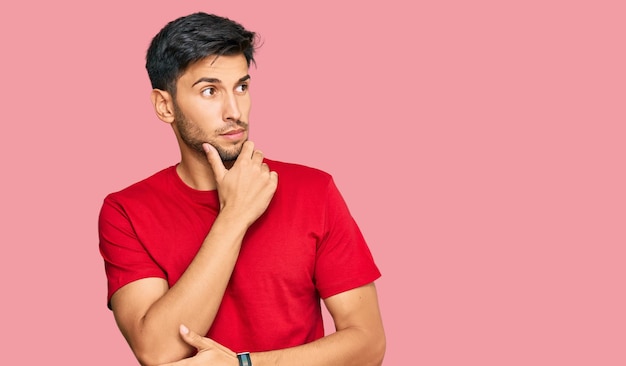 Hombre guapo joven con camiseta roja casual pensando preocupado por una pregunta preocupada y nerviosa con la mano en la barbilla