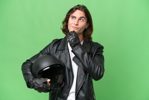 Hombre guapo joven con un casco de motocicleta aislado sobre fondo de croma verde y mirando hacia arriba