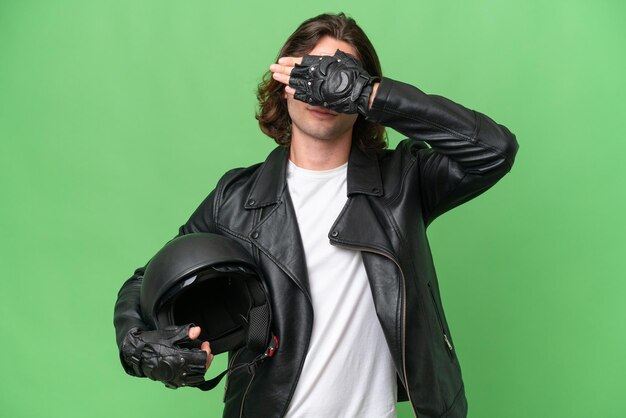 Hombre guapo joven con un casco de motocicleta aislado sobre fondo de croma verde que cubre los ojos con las manos No quiero ver algo