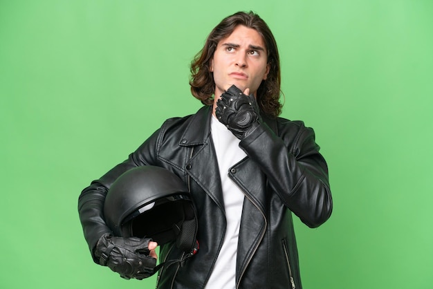 Hombre guapo joven con un casco de motocicleta aislado sobre fondo de croma verde que tiene dudas y pensamiento