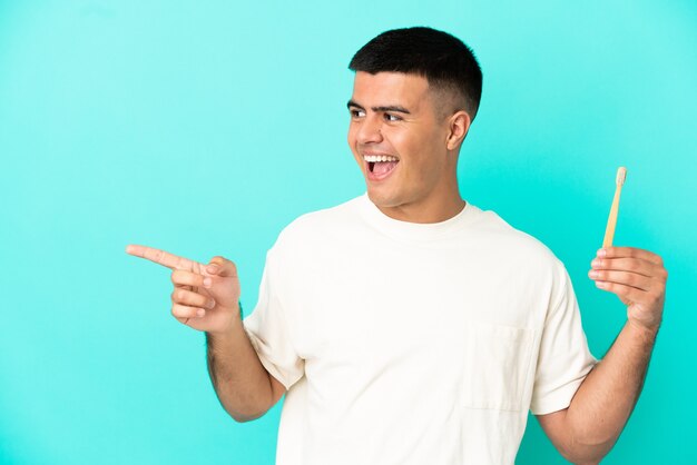 Hombre guapo joven cepillarse los dientes sobre fondo azul aislado apuntando con el dedo hacia el lado y presentando un producto