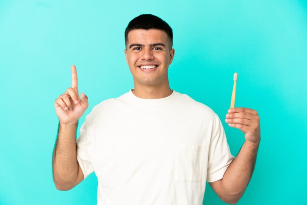 Hombre guapo joven cepillarse los dientes sobre fondo azul aislado apuntando hacia una gran idea