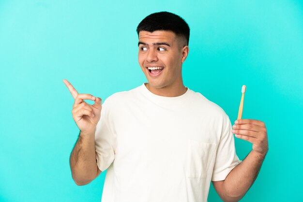 Foto hombre guapo joven cepillarse los dientes sobre fondo azul aislado con la intención de darse cuenta de la solución mientras levanta un dedo hacia arriba