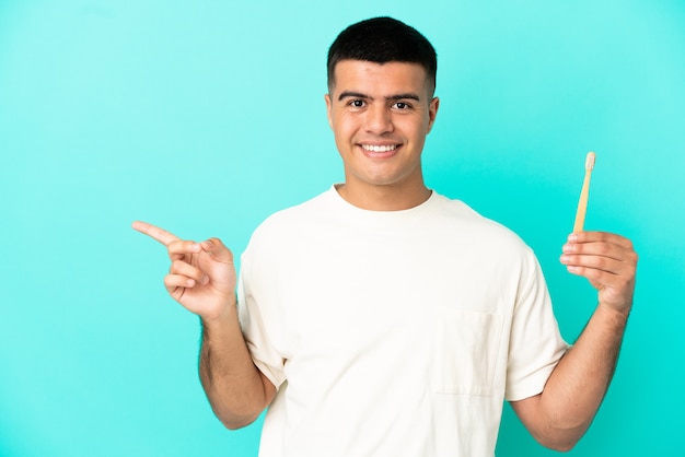 Hombre guapo joven cepillarse los dientes sobre la pared azul aislada que señala el dedo hacia el lado