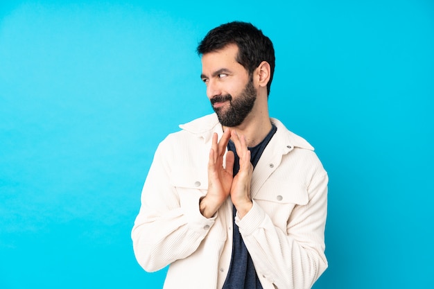 Hombre guapo joven con chaqueta de pana blanca sobre pared azul aislada intrigando algo