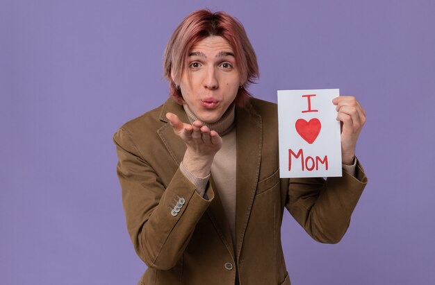 Hombre guapo joven complacido sosteniendo una carta para su mamá y enviando un beso