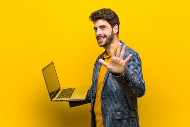 Hombre guapo joven con una computadora portátil contra el fondo naranja