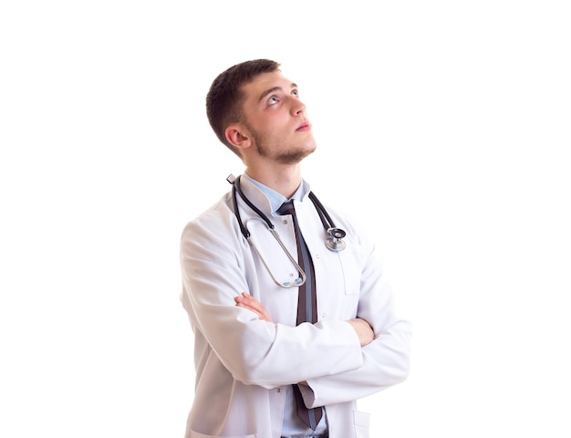 Hombre guapo joven con corbata de camisa azul y bata de médico con estetoscopio en el cuello pensando