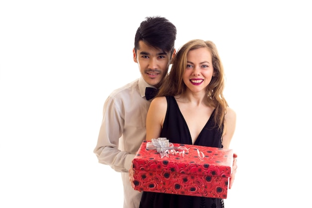 Hombre guapo joven con corbatín negro y mujer hermosa en vestido negro con regalo rojo