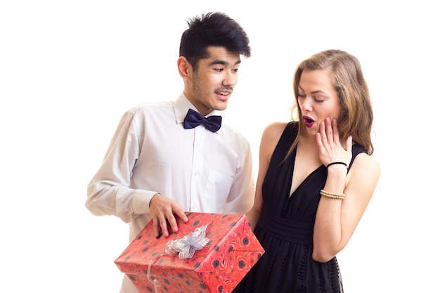 Hombre guapo joven con corbatín negro y mujer hermosa en vestido negro con regalo rojo