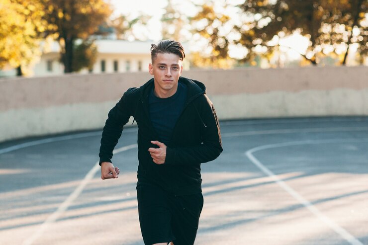 Foto hombre guapo joven corriendo por la pista del estadio.