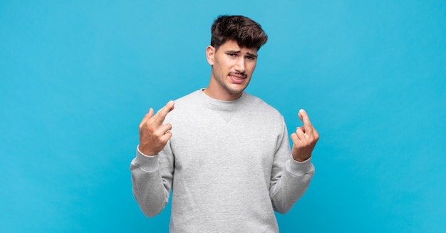 Hombre guapo joven cruzando los dedos con ansiedad y esperando buena suerte con una mirada preocupada