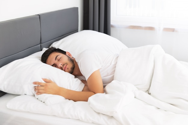 Foto hombre guapo joven durmiendo en su cama.