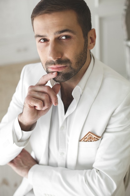 Hombre guapo joven elegante con barba en un traje clásico blanco