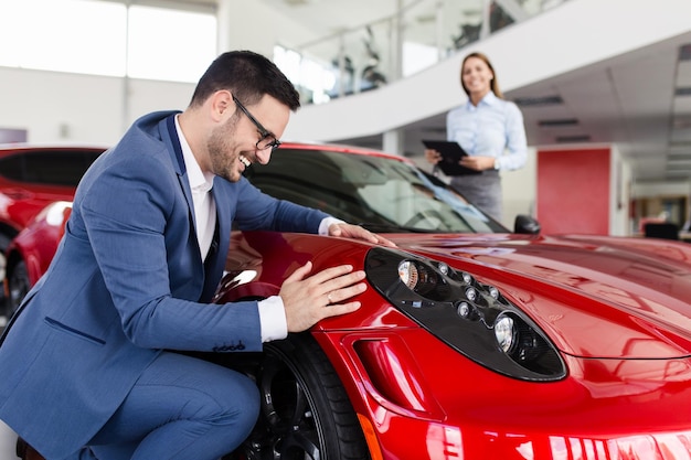 Hombre guapo joven eligiendo un auto nuevo en la sala de exposición de autos.