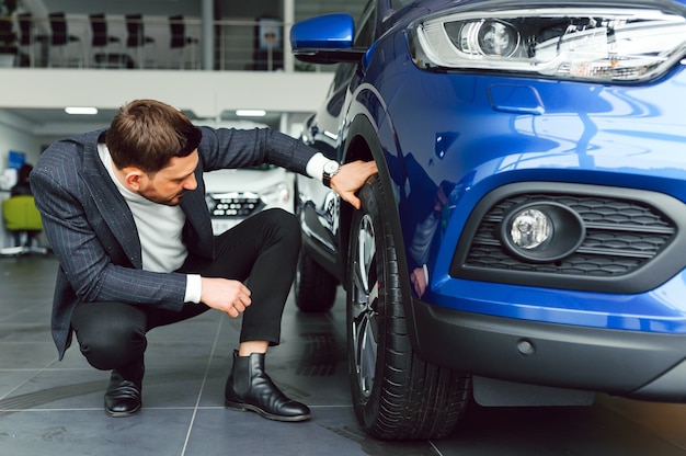 Hombre guapo joven eligiendo un coche en una sala de exposición de coches