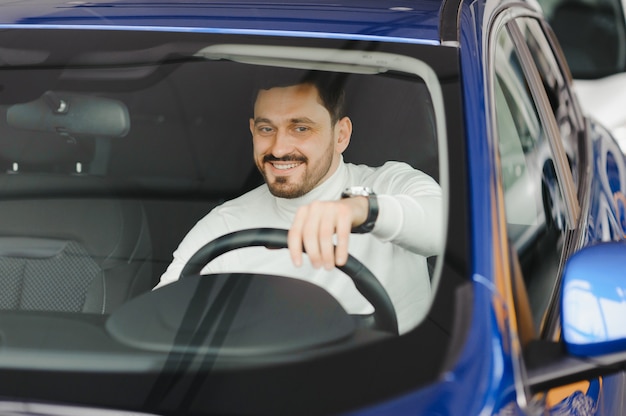 Hombre guapo joven eligiendo un coche en una sala de exposición de coches