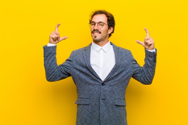 Foto hombre guapo joven enmarcando o esbozando su propia sonrisa con ambas manos, mirando positivo y feliz, concepto de bienestar contra la pared naranja