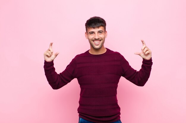 Hombre guapo joven enmarcando o esbozando su propia sonrisa con ambas manos, mirando positivo y feliz, concepto de bienestar contra la pared rosa