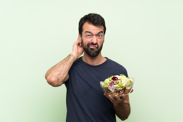 Hombre guapo joven con ensalada sobre pared verde aislada con dudas