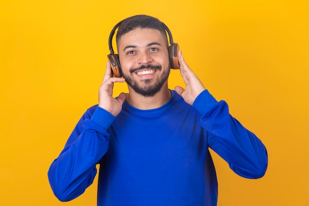 Hombre guapo joven escuchando música en auriculares fondo de estudio amarillo aislado sonriendo feliz