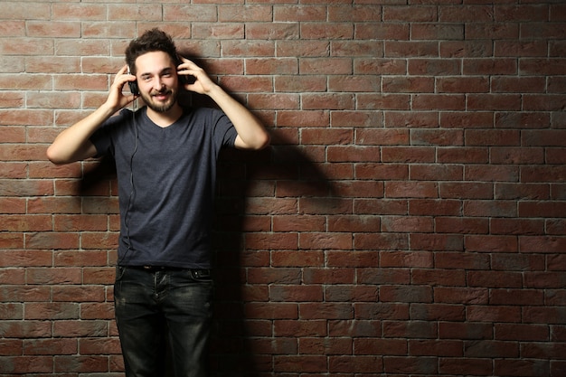 Hombre guapo joven escuchando música con auriculares en la pared de ladrillo