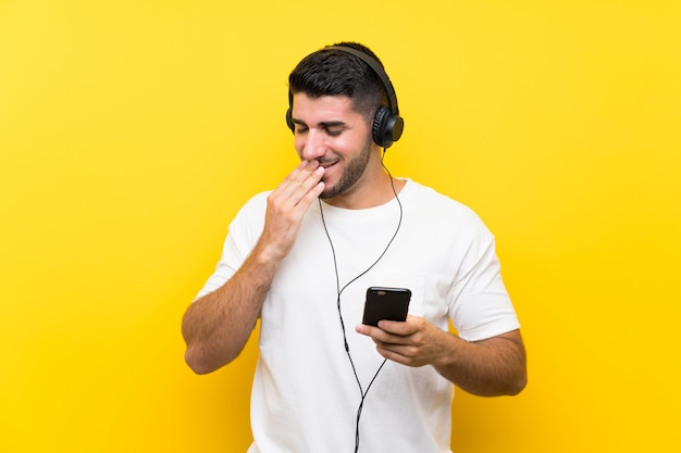 Hombre guapo joven escuchando música con un móvil sobre pared amarilla aislada sonriendo mucho