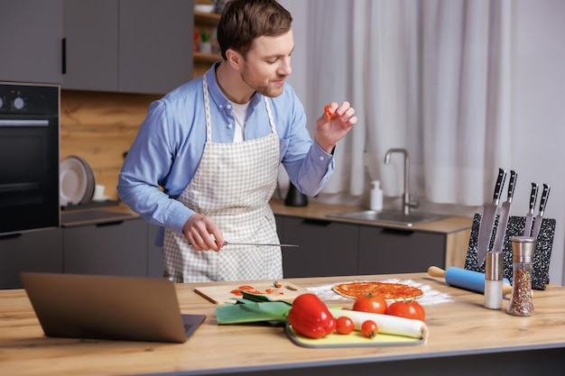 Hombre guapo joven está preparando pizza y ensalada en la cocina El hombre disfruta el proceso de cocción
