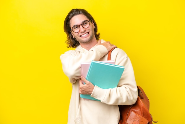 Hombre guapo joven estudiante aislado sobre fondo amarillo riendo
