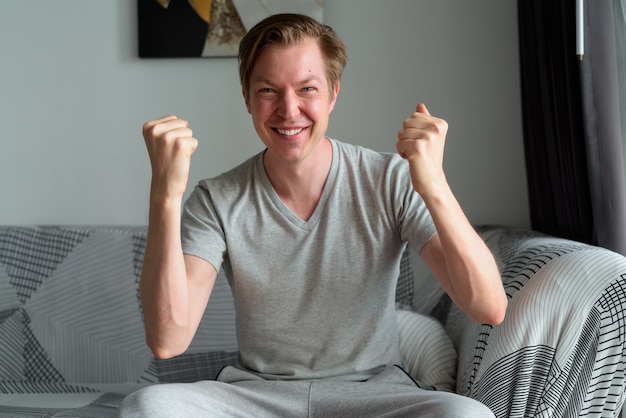 Hombre guapo joven feliz recibiendo buenas noticias en la sala de estar en casa