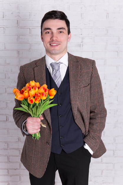 Hombre guapo joven con flores sobre pared de ladrillo blanco