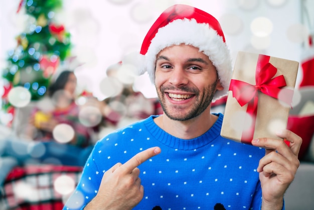 Hombre guapo joven con un gorro de Papá Noel con un regalo de Navidad