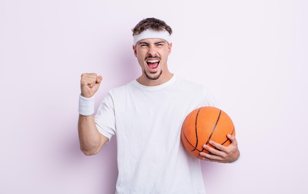 Hombre guapo joven gritando agresivamente con un concepto de baloncesto de expresión enojada
