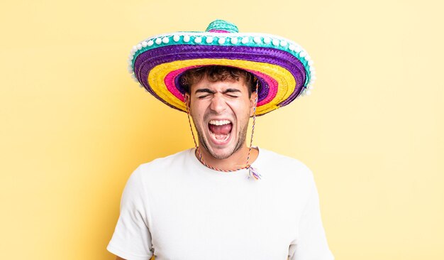 Hombre guapo joven gritando agresivamente con un concepto de sombrero mexicano muy enojado