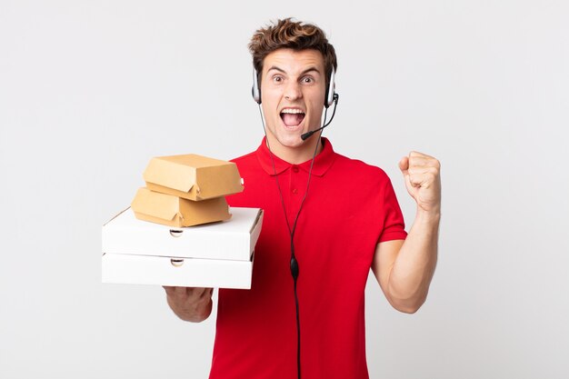 Hombre guapo joven gritando agresivamente con una expresión enojada. llevar concepto de comida rápida