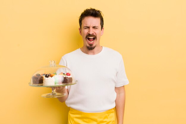 Hombre guapo joven gritando agresivamente luciendo muy enojado concepto de pasteles caseros