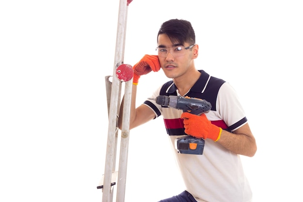 Hombre guapo joven con guantes y gafas protectoras con destornillador eléctrico gris y ledder